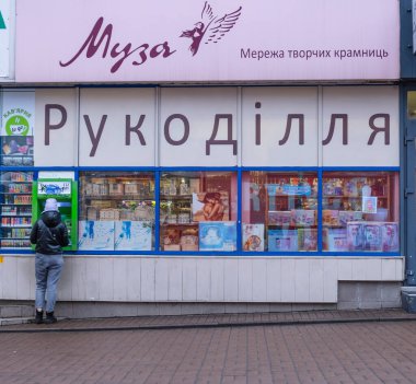 Kyiv, Ukrayna - 19 Kasım 2021: Şehir caddesinde otomatikleştirilmiş bir veznedarla etkileşime giren kişi, arkasında çeşitli yaratıcı öğeleri gösteren bir el işi dükkanı penceresi