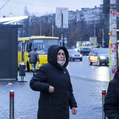 Kyiv, Ukrayna - 19 Kasım 2021: Bir şehir caddesinde dikilen kadın, soğuk bir günde çevreyi gözlüyor ya da bekliyor, kentsel yaşamı ve günlük trafiği gösteriyor
