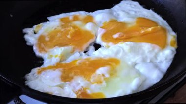 Sıcak yağda pişen ve cızırdayan üç yumurta ile yakın çekim siyah dökme demir tavada, protein zengini bir kahvaltı için basit ve hızlı bir ev yemeği hazırlama