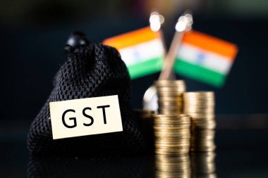 Arka plan olarak Bozuk Para ve Hint bayrağı yığınının önünde GST etiketi olan çanta - Hindistan 'da mal ve hizmet dolaylı vergi tahsilatı kavramı