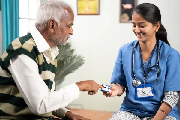 Selective focus on girl, Concept of home health visit or service - doctor or nurse checking pulse using pulse oximeter of sick senior man while both worn face mask. — Stock Photo, Image