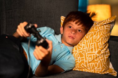 Yalnız genç bir çocuk gece geç saatlerde oyun oynarken joystick kullanıyor. Çocukların oyun bağımlılığı ve gece geç saatlerde oyun oynama kavramı.