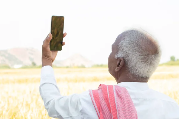 Concept of mobile phone network reception or signal problem - Elderly Indian farmer searching for good network signal near the agriculture land at village