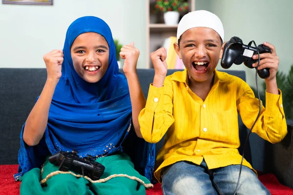 Point of view shot, Two muslim kids cheering and shouting after won the online video game while playing with joystick or gamepad at home sitting on sofa
