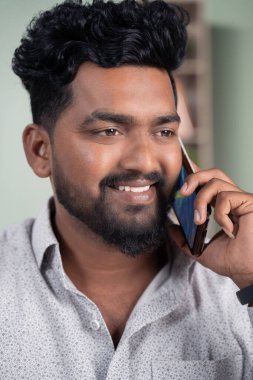 Gülümseyen genç Hintli adamın cep telefonuyla konuşmasına ya da konuşmasına yakın durun..