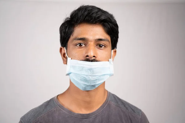 young man wearing medical mask below nose - concept showing of improper way of using face masks during coronavirus or covid-19 crisis.