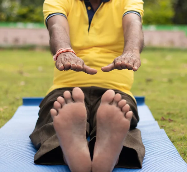 Low-angle view of unrecognizable old man sitting down on exercise or yoga mat touching his toes - Concept of active happy elderly health and fitness.