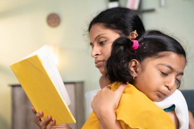 Anne kitap okumakla ve çocuğunu evde uyutmakla meşgulken kız çocuk annesinin omzunda uyuyor.