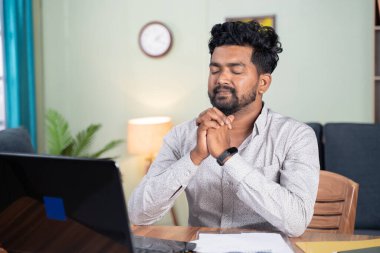 young man praying in front of laptop after completion of online test or examination for results - Concept of believe and gratitude