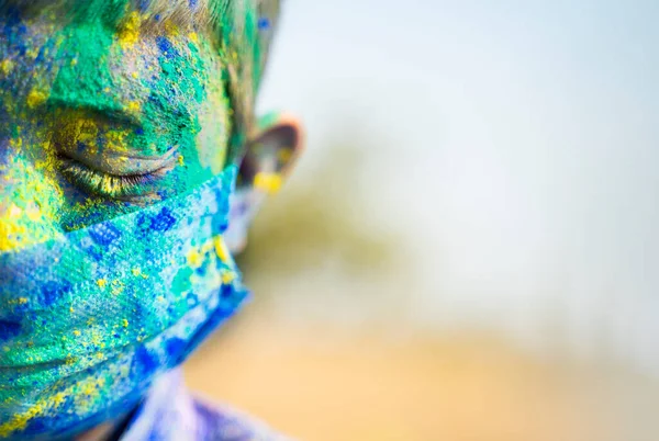 Close up half face head shot of Young boy with medical face mask played holi the festival of colours and looking into camera - concept of holi celebration during covid-19 coronavirus pandemic