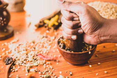 Ellerin ahşap kasedeki Hint baharatlarına ya da Hint masala baharatlarının hazırlık konseptine vurması ya da kırması.