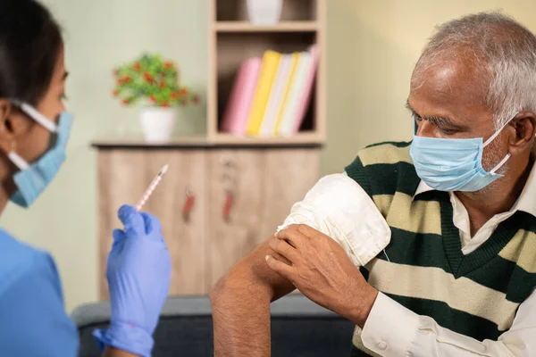 Doktor yaşlı hastaya şırınga ya da mahkeme kararıyla aşı yaptıktan sonra, hastanın evde omzunu ovması - Coronavirus covid-19 aşısı sırasında yaşlılara ev sağlığı kontrolü kavramı.