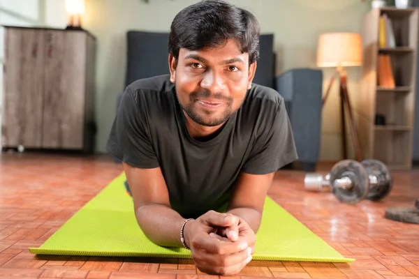 Young man with smiling face on yoga mat at home after working out looking camera, concept of home gym, new normal lifetyle, health and fitness