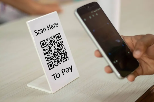 Focus on Scan here to pay text, Close up of hands Scaning QR code for digital contact less payment after shopping - concept of technology, safety and privacy.