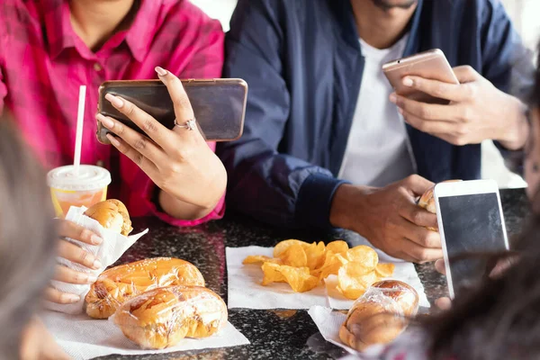 Group of unrecognizable people busy on mobile while having snacks together at restaurant - Concept of millennials having junk food, phone addiction, social media sharing and connection