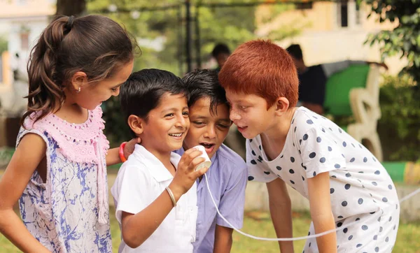 group of children having fun by playing with String Telephone during holiday summer camp - Concept of brain development and socializing by playing outdoor games in the technology driven world.