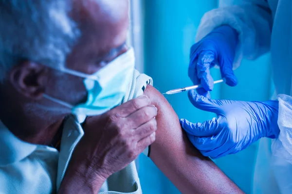 Senior elderly patient with mask getting vaccination or jab at hospital - Doctor in protective Hazmat suit treating Covid patient injecting anti-viral vials at covid care Centre —  Fotos de Stock