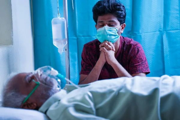 병원에서 호흡기 마스크를 착용하면서 아버지가 회복되기를 기도하는 젊은이를 걱정하며 스트레스를 — 스톡 사진