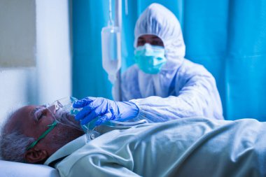 Coronavirüs akciğer enfeksiyonu nedeniyle hastalara nefes almakta zorlanan solunum yolu enfeksiyonuna karşı havalandırma oksijen maskesi takmaya yardımcı olan doktor hazmat veya koruyucu giysi