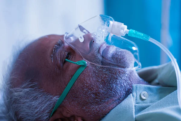 Close up head shot side view of old man breathing with ventilator oxygen mask at hospital due to coronavirus covid-19 lung infection, breath shortness or dyspnea.