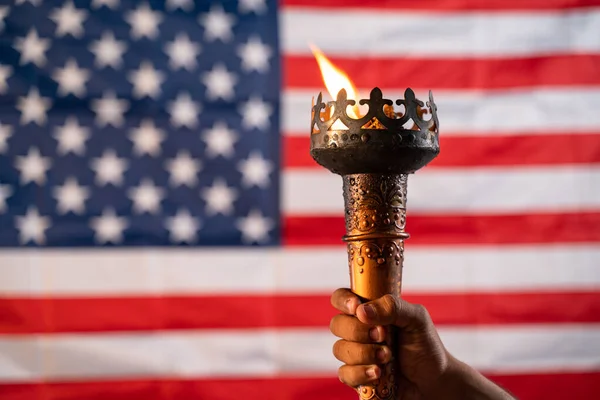 Fechar as mãos segurando tocha de chama olímpica com bandeira americana ou americana como fundo — Fotografia de Stock