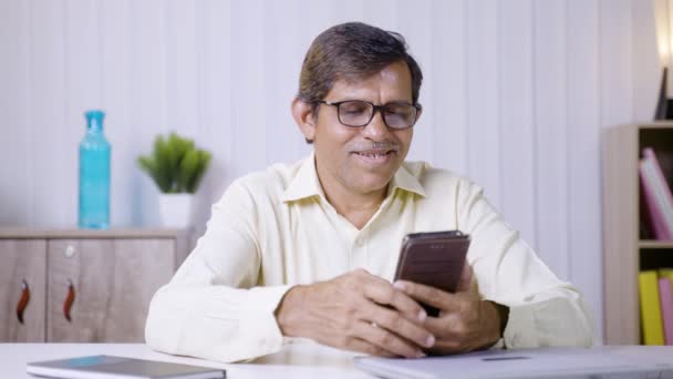 Middle aged businessman smiling while using mobile phone at office - concept of using social media, internet, checking mails and communication at workplace — Stock Video