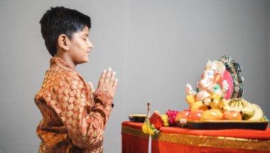 Ganesha Festivali 'ndeki çocuğun atölye fotoğrafı. Geleneksel elbise gri arka planda Ganapati heykelinin önünde dua ediyor.