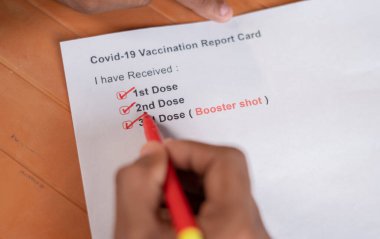 POV close up shot of hands checking Covid-19 vaccine report card and ticking 3rd or booster dose after vaccination. clipart