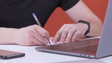 Akşam iş belgeleriyle çalışan genç bir iş adamı. Genç Avrupalı bir adam dizüstü bilgisayar kullanıyor, bir girişimde bulunuyor, Parlak Kırmızı Ofiste İş İnterneti Kalemle Yazıyor