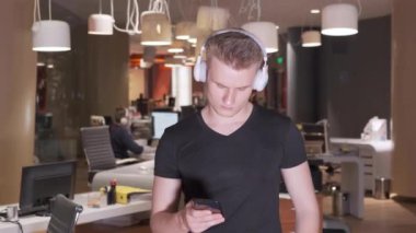 Kulaklık takan genç bir Avrupalı gecenin geç saatlerinde boş bir ofiste akıllı telefon kullanarak müzik dinliyor.