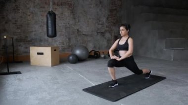 Siyah taytlı, seksi, esmer, genç bir kız spor salonunda paspas üzerinde egzersiz yapıyor. Spor ve spor eğitimi alıyorum. Sağlıklı bir yaşam tarzı. Uzanıyor, öne eğiliyor.