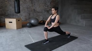 Siyah bluzlu ve taytlı genç Hintli kadın esneme hareketleri yapıyor, spor salonunda egzersiz yapıyor.