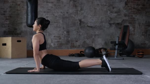 一个年轻的女运动员在体育馆的垫子上训练 在黑色背景下为女孩做伸展运动 — 图库视频影像