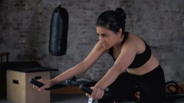 Bisiklet sınıfında statik bisiklete binen Hintli bir kadının portresi. Spor salonunda spor yapan kadın bisiklet çeviriyor..