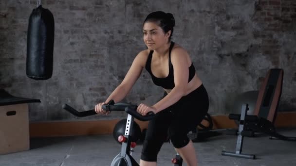 アクティブ若いアジアの女性サイクリング運動自転車でジムで楽しい 心臓脂肪燃焼トレーニングプログラム 自然光 — ストック動画