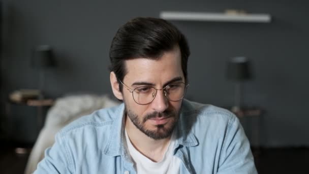 暗い部屋で自宅でコンピュータで働くメガネを持つ若いヨーロッパ人の思考の男の閉鎖 — ストック動画