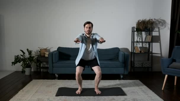 一个年轻的体育男子在家里做跳跃蹲大腿锻炼 一个强壮的男性训练来调理客厅里的皱纹 散乱的腿肌肉 体育和丰富的生活方式概念 — 图库视频影像
