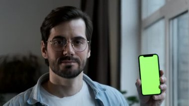 Gözlüklü bir adamın Yeşil Ekran Çevrimiçi ile Smartphone kullandığını, Evde Bir Pencere Yakınında Durduğunu,