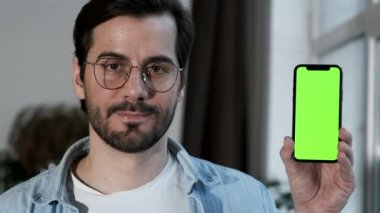 Gözlüklü bir adamın Yeşil Ekran Çevrimiçi ile Smartphone kullandığını, Evde Bir Pencere Yakınında Durduğunu,