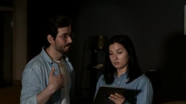 Couple using mobile tablet devices, A young woman and man are working in their living room in the dark background