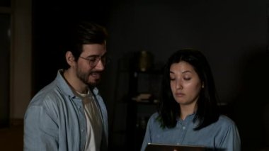 Close up A young woman and man are working in their living room in the dark background, Two Managers Working from Home, Using a Tablet