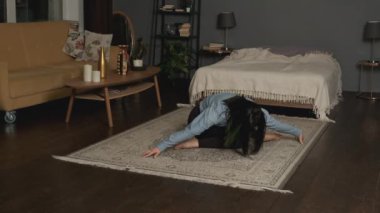 Young woman has workout at home during quarantine. She stretching forward and bending her back in yoga pose