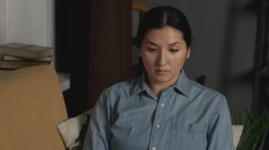 Footage of beautiful young asian woman working with laptop at home, Works and Communicates with Friends or a Client Online, Sits on the Couch, Uses a Laptop In a Dark Room at Home