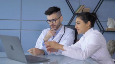 İki doktor, bir erkek ve bir kadın, tablet ekrana bakıyorlar ya da bilgisayar ya da dizüstü bilgisayarda çalışıyorlar.