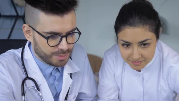 两名医生的特写镜头 一名男医生和一名女医生在明亮的医院办公室里 他们正在看平板电脑或笔记本电脑 — 图库视频影像