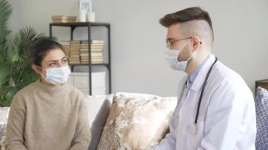 Maskeli genç bir erkek doktor Hintli bir hastayla konuşuyor, bir kadın virüslü, evinde, parlak bir odada.