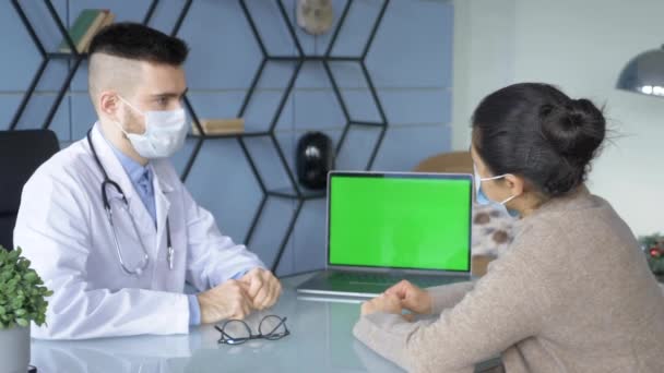专业男医生填写数据 用绿色屏幕在电脑上填写医疗报告 漂亮的成年妇女坐在医生旁边 在医院房间等着 — 图库视频影像