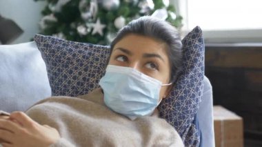 Maskeli, ekoseli bir odada kanepede yatan ve üşümüş Hintli bir kadını yakından çek. Genç, güzel, hasta bir kadın kendini kötü hissediyor. Salgın virüs enfeksiyonu. Hastalık konsepti
