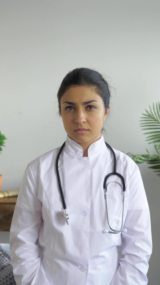 明るい部屋 ウイルス病とパンデミックの時間 垂直ビデオに身を包んだカメラを見ている若いインドの深刻な女性医師の肖像 — ストック動画