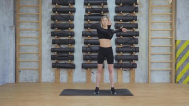 El egzersizi yapan genç bir kız, spor salonunda çalışmak için kaslarını esneten, siyah spor kıyafetleri giyen bir kız.